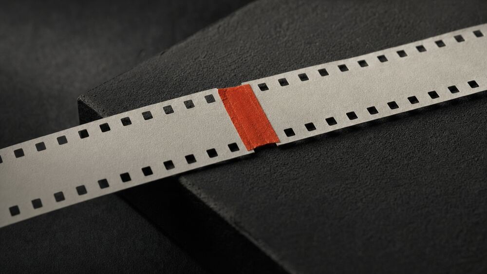 Macro detail of two lengths of blank film leader spliced together with a strip of red tape on a cutting block.