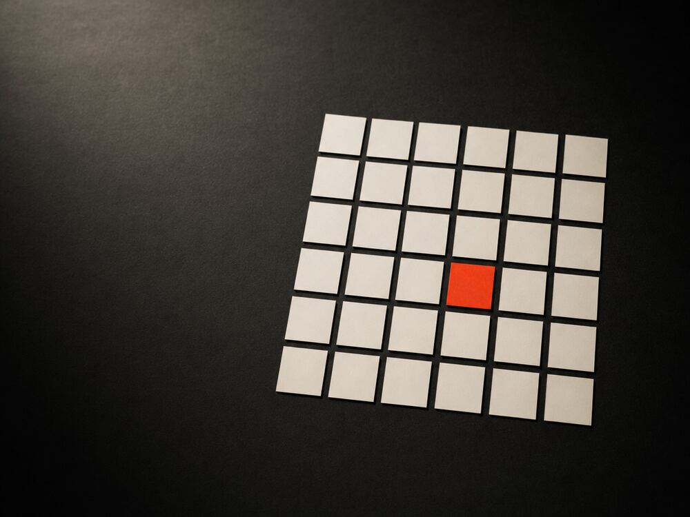An orderly grid of small blank white cards on a dark surface, with a single card replaced by a red one.