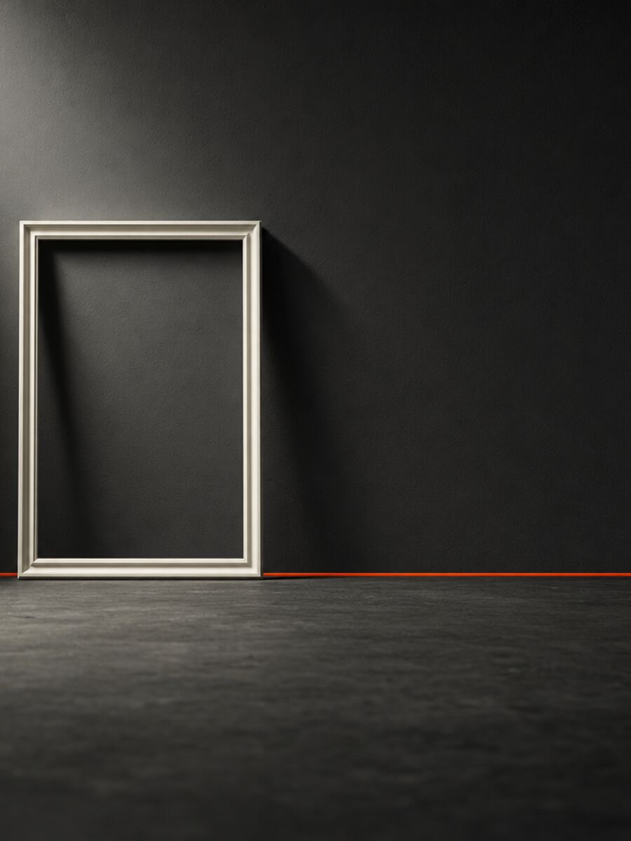 A single empty white frame standing against a dark wall, lit hard from the left, casting a long clean shadow. Nothing inside it.